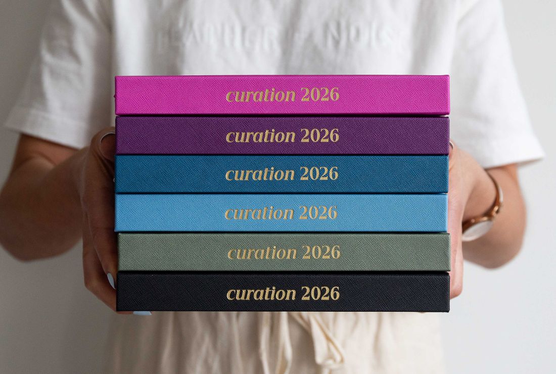 Stack of curation 2026 diary held by a person against a neutral background